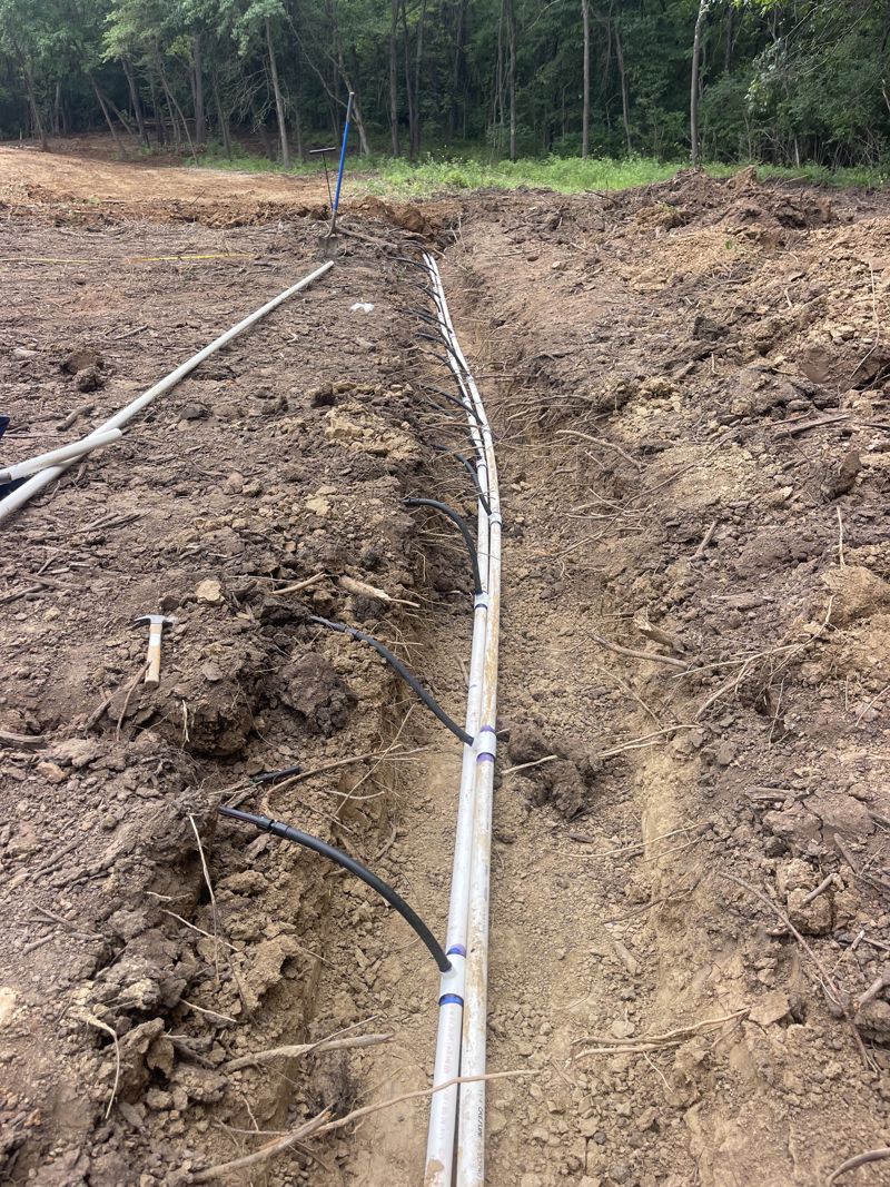 Septic lids and control panel post in freshly graded dirt beside a green farmhouse