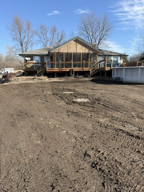 Freshly graded yard after a septic tank replacement, with septic lids behind a ranch home with a wood deck